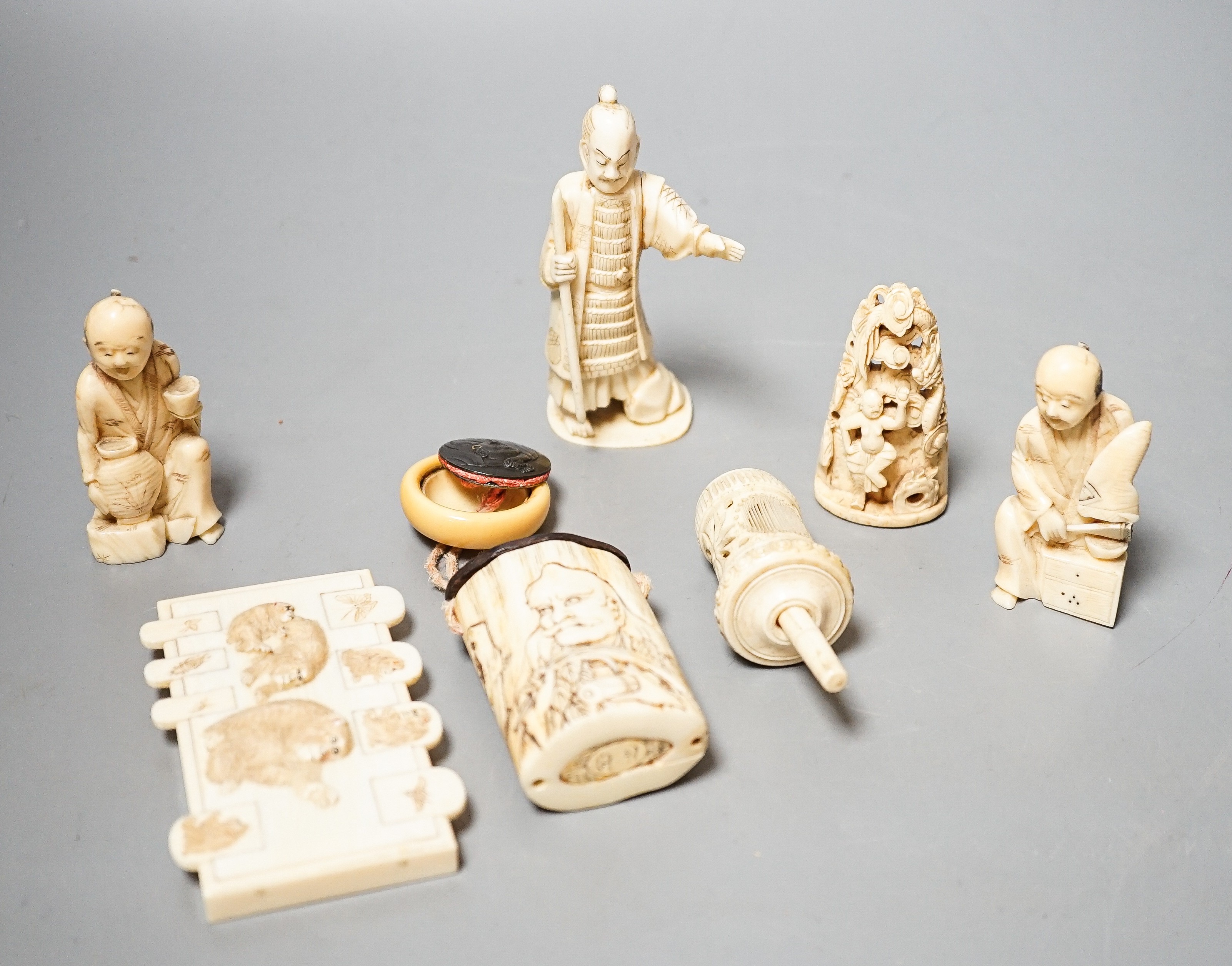 Three Japanese Ivory figures of men, a similar bezique marker, a Japanese staghorn single section inro with ivory manju, a Chinese ivory carving and a bone needlework container